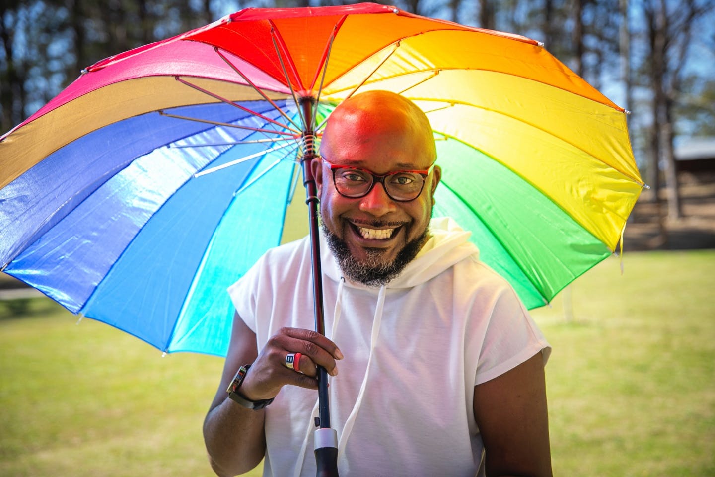 Uomo di razza nera che vive con l'HIV negli Stati Uniti sorride e tiene in mano un grande ombrello con i colori dell'arcobaleno